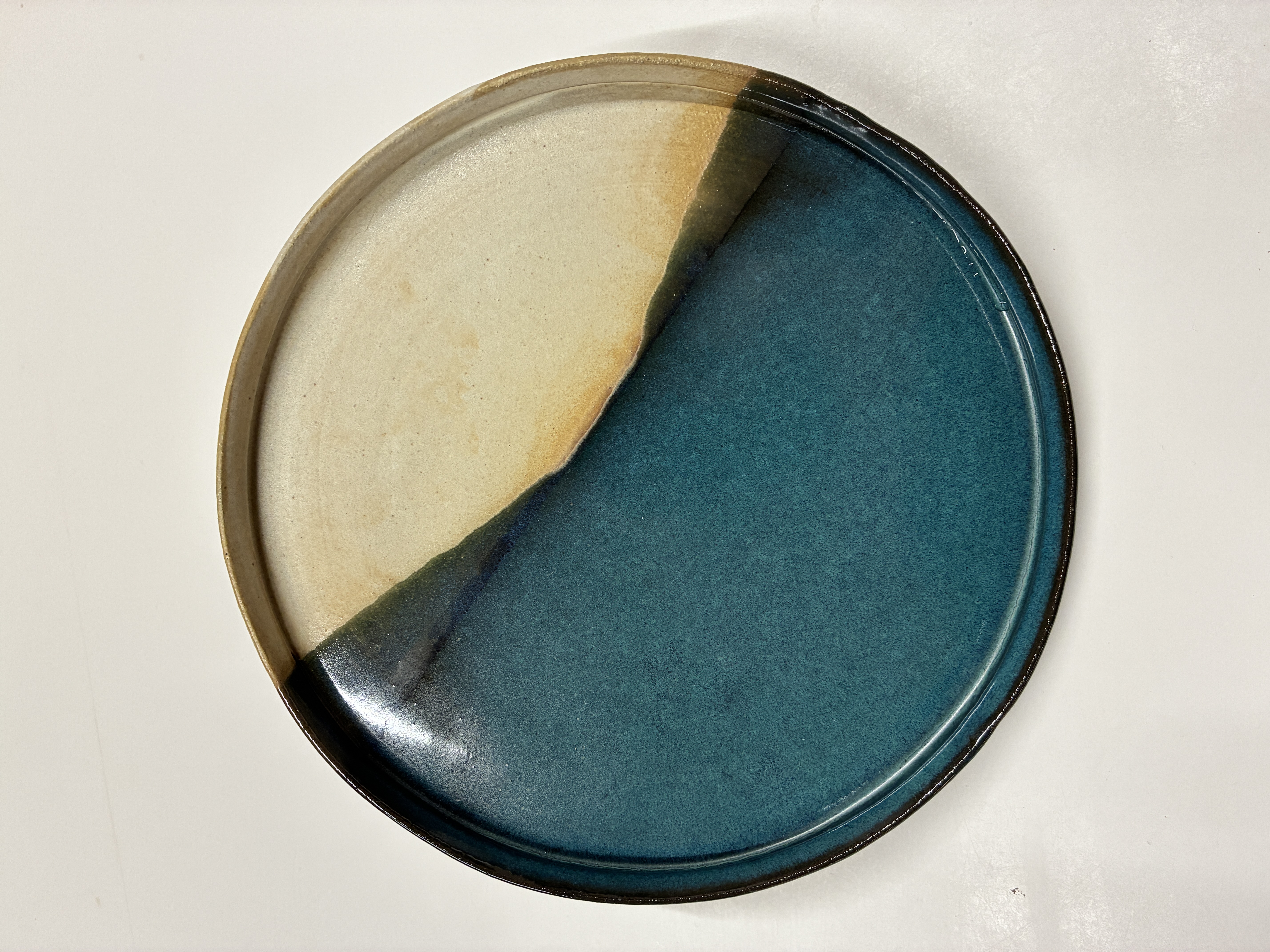 A plate with raised sides. The plate is a shimmering green with a clock-face of off-white that blends with dark orange shades so the effect is like a sunset.